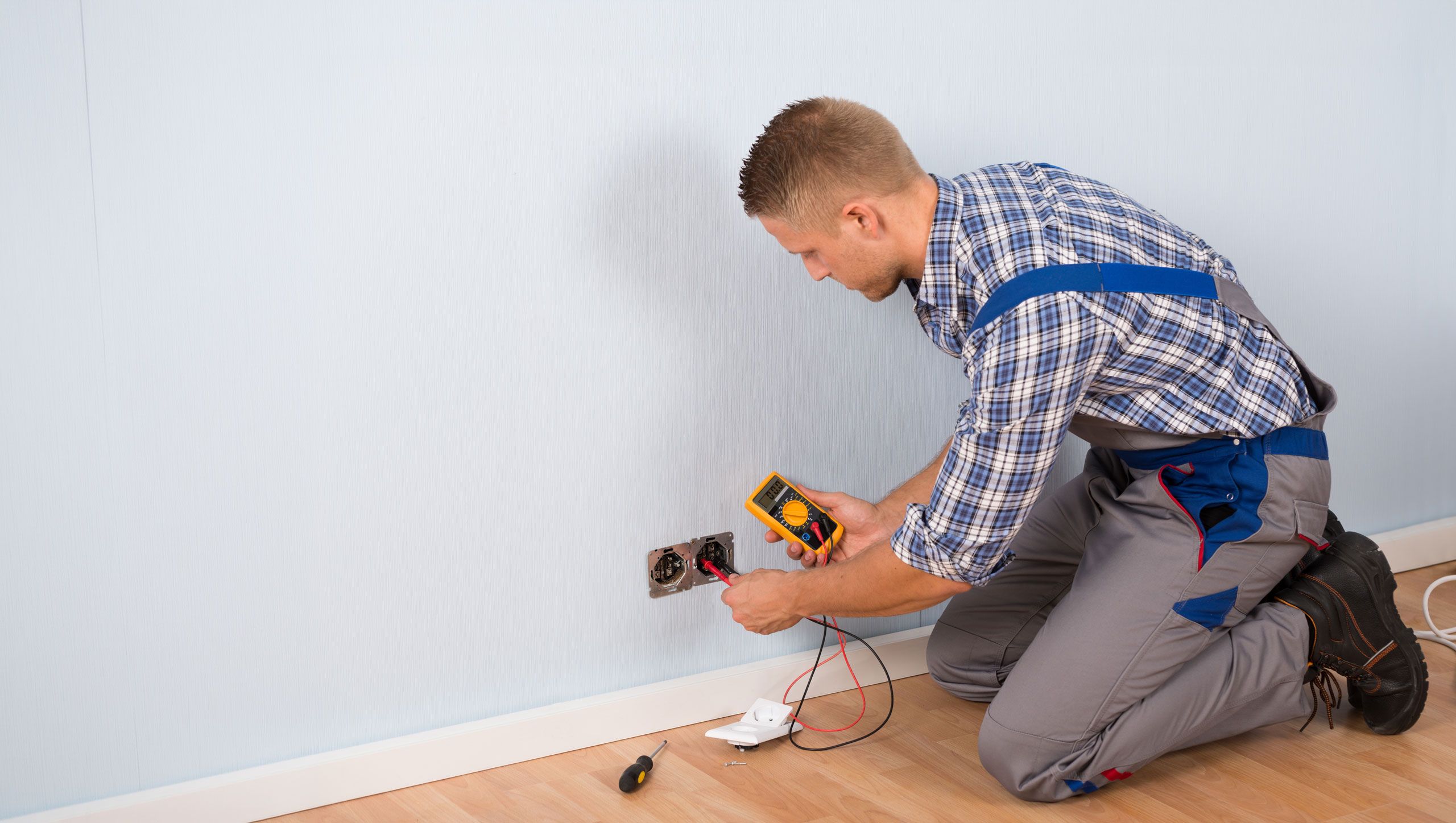 Elektriker prüft die Spannung einer Steckdose an der Wand mit einem Multimeter